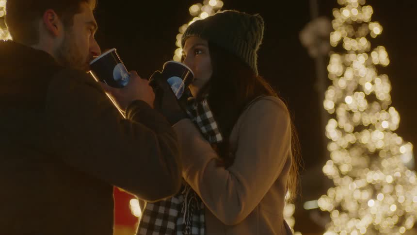 A couple drinks a hot drink while bundled up outside