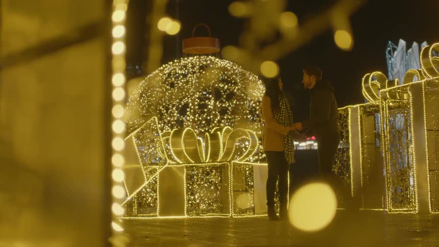 A man proposes to his girlfriend as they walk hand in hand through a holiday light display