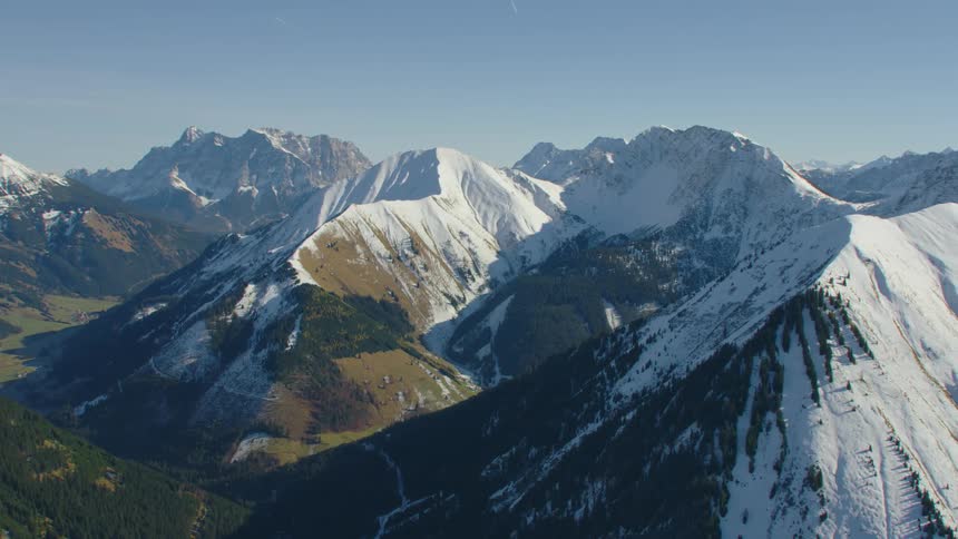 Bright sunlight shines down on a mountain range dusted with snow