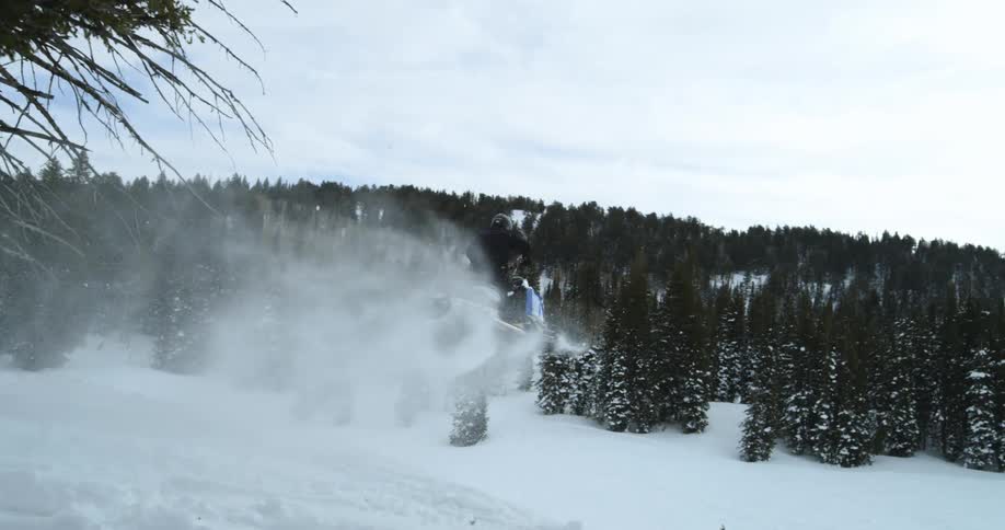 A snowmobile jumps down the hill of a mountain slope
