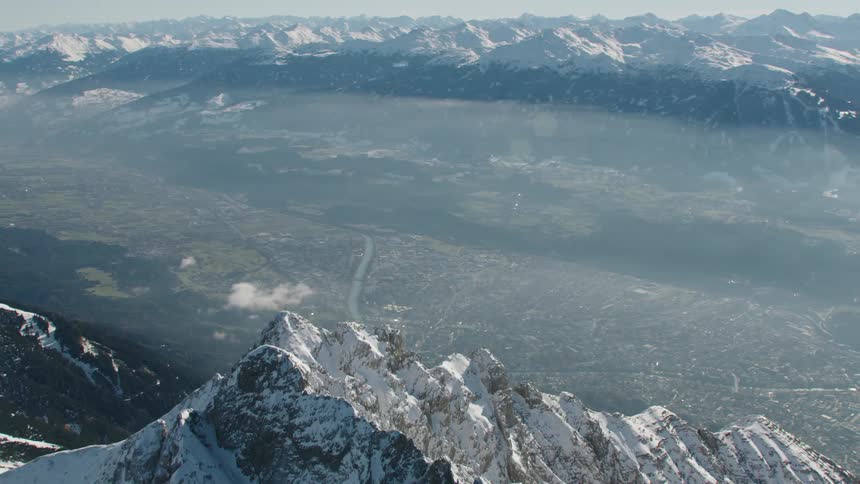 Aerial view of steep snowy mountain and distant town in valley