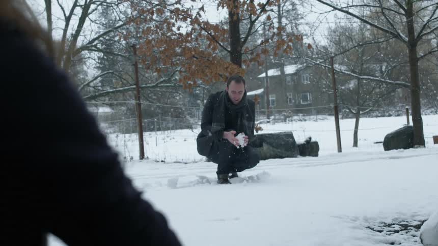 A man is making a snowball as it snows