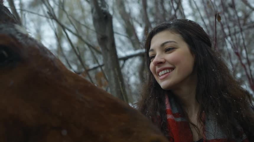 A woman is petting a horse as it snows