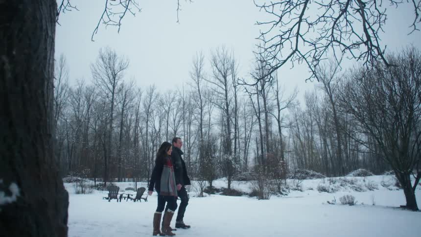 A man and women walk in the snow by a forest