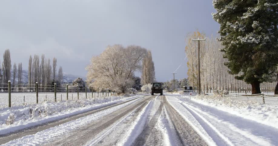 A farm vehicle drives down the snow covered road