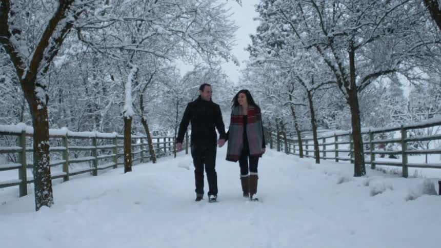 A man and woman hold hands as they walk in the snow