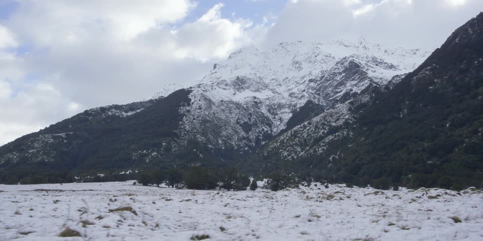 Snow covers a mountain and the ground in front of it