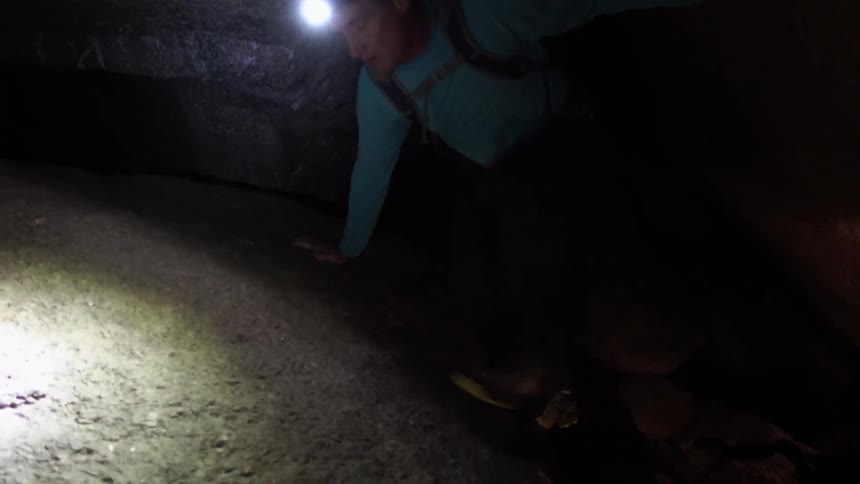 A person wearing a headlamp climbs a rocky tunnel