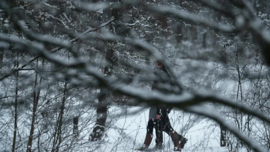 A man and women are walking in a forest covered in snow