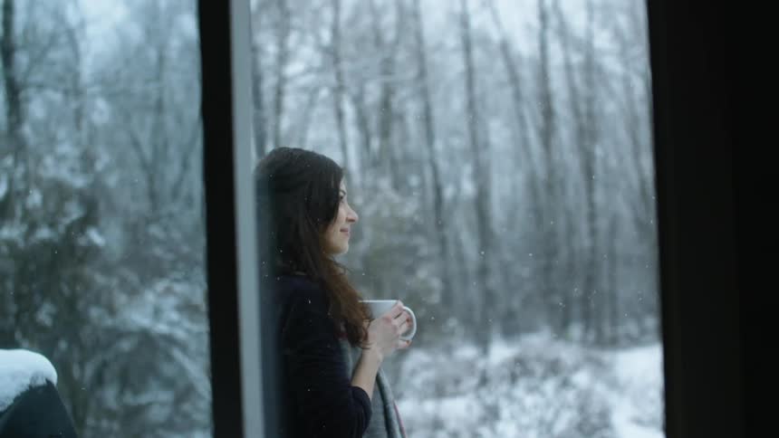 A woman holding a mug stands outside in the snow