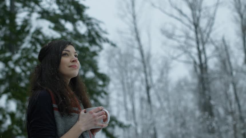 A woman stands outside holding a mug in the snow