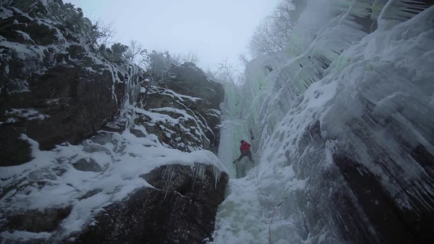A climber is navigating a wall of ice on a cliff