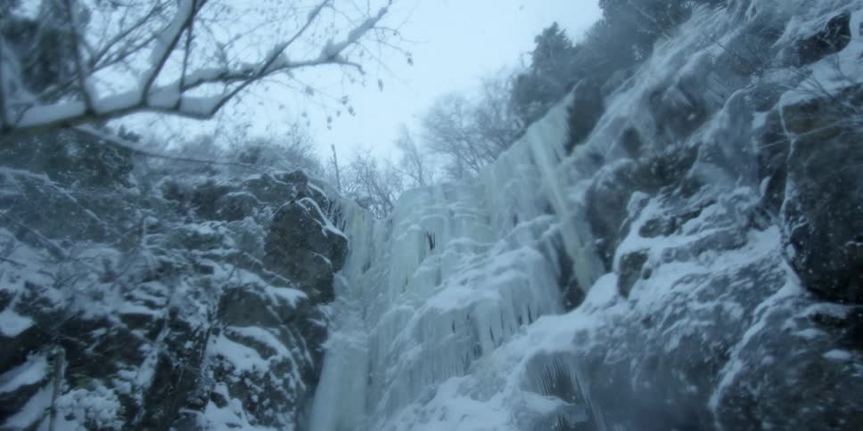 The snow is falling around this cliff with ice over the edge