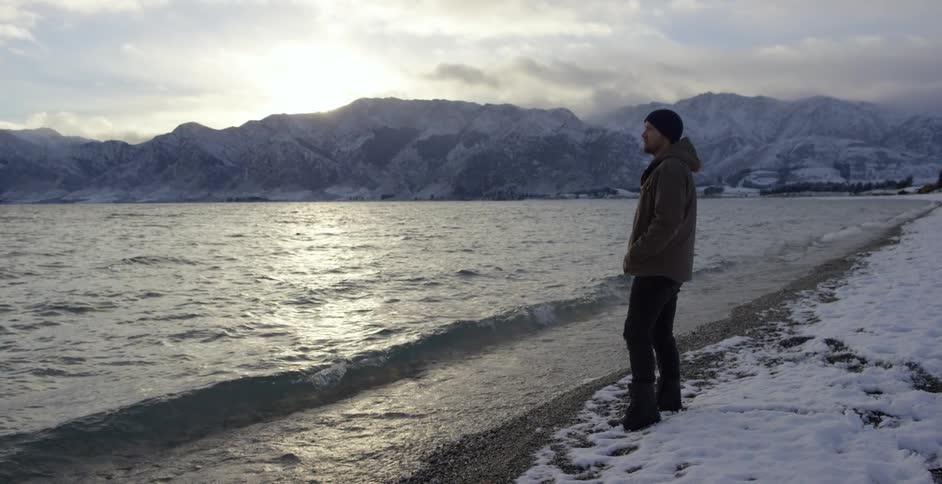 Man standing on a snowy beach looking at the water