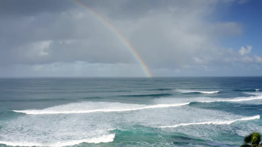 A rainbow appears in clear blue sky over the ocean