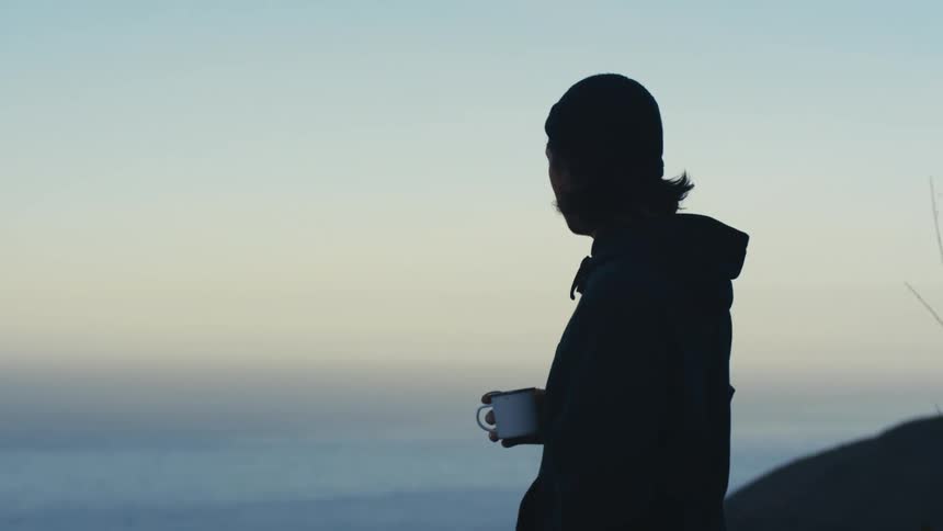Person drinking from mug on hill