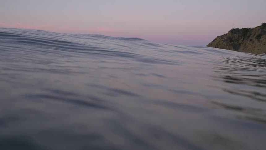 Wave swells on ocean surface near shore under red sky