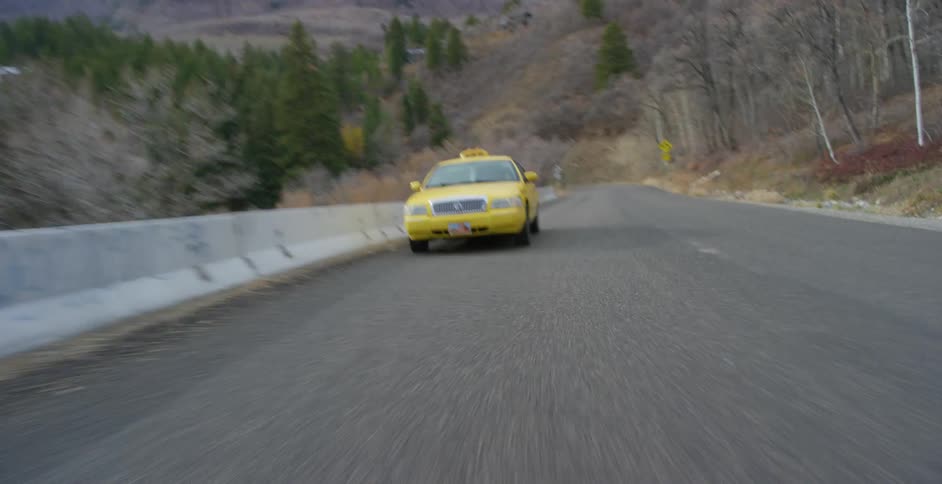 A yellow taxi is traveling on a mountain road with mountains in the distance