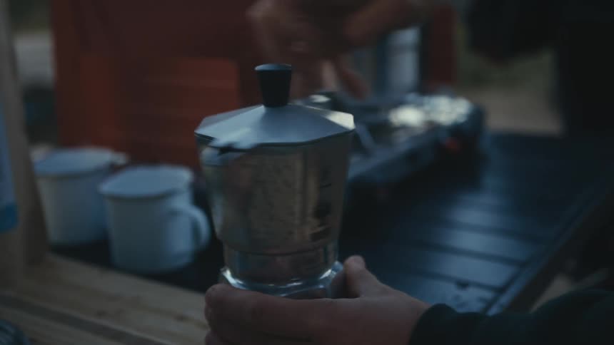 Someone screws the top onto a tea pot and puts it on a burner