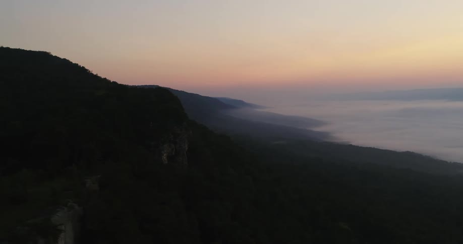 Waves roll onto a beach below a hill under a colorful hazy sky