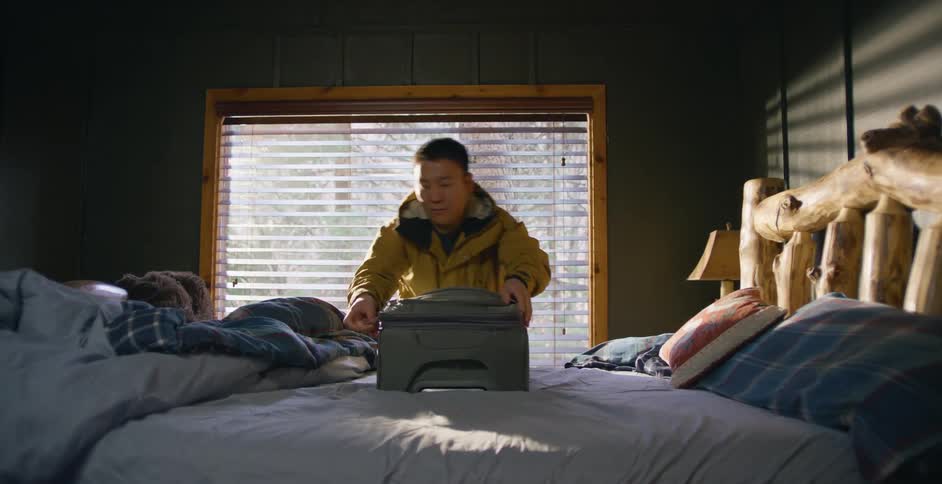A man is rushing to put clothes in a suitcase before zipping it shut and carrying it away