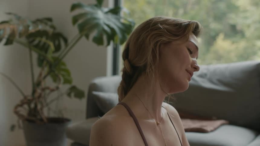 A woman sits on the floor in her living room and moves her head to side to side as she stretches