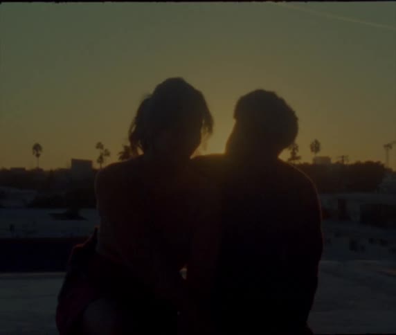 A woman leans in toward her boyfriend with the sunset back lighting them