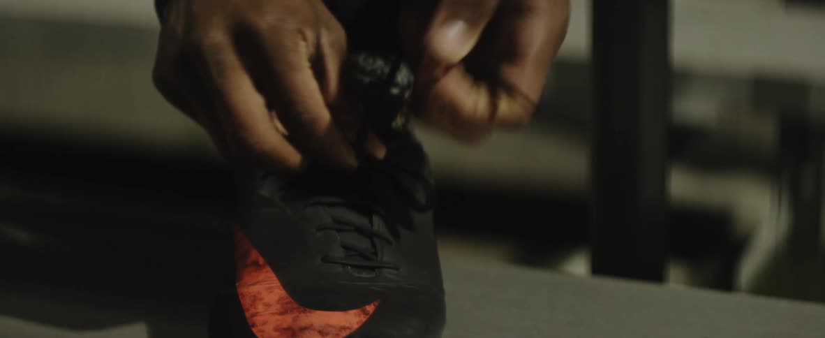 A close view of an athlete tying the shoelaces of athletic footwear with cleats in the daytime