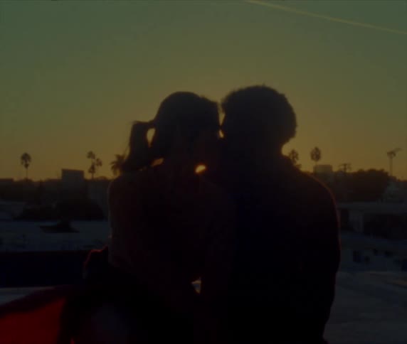 The silhouette of a couple kissing with the sun shining between them at sunset
