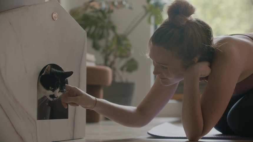 Woman kneels on mat petting car standing in door of small pet house