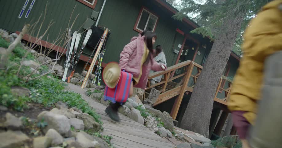 Parents rush children along as they leave building with luggage walking past skis and conifers