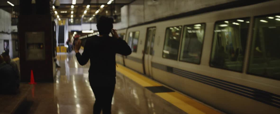 A subway train pulls into a station while a person dances on the platform