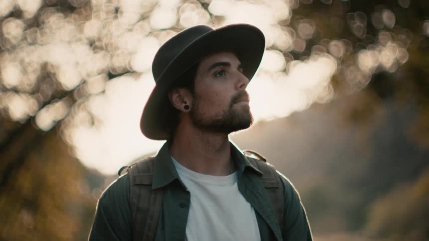 A man stands under trees in a forest area and looks around