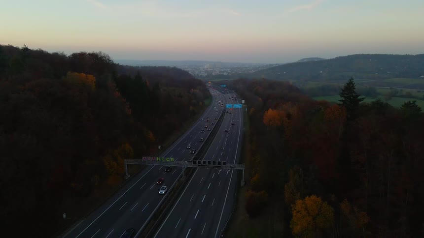 Traffic travels along a highway through a forest in the evening