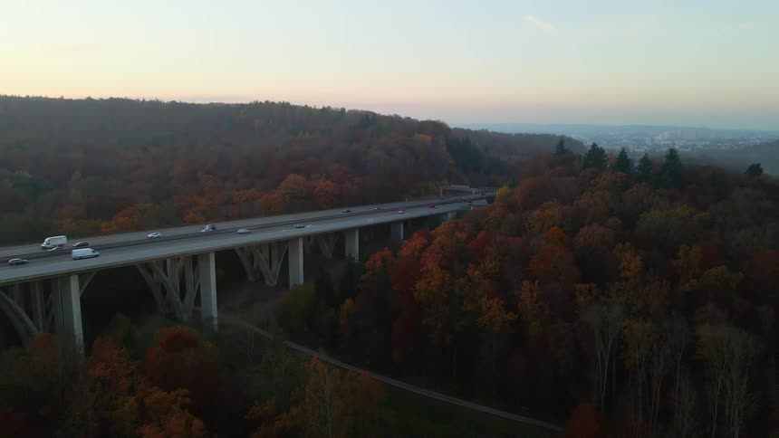 Heavy traffic passes along a highway surrounded by trees and leading in and out of downtown