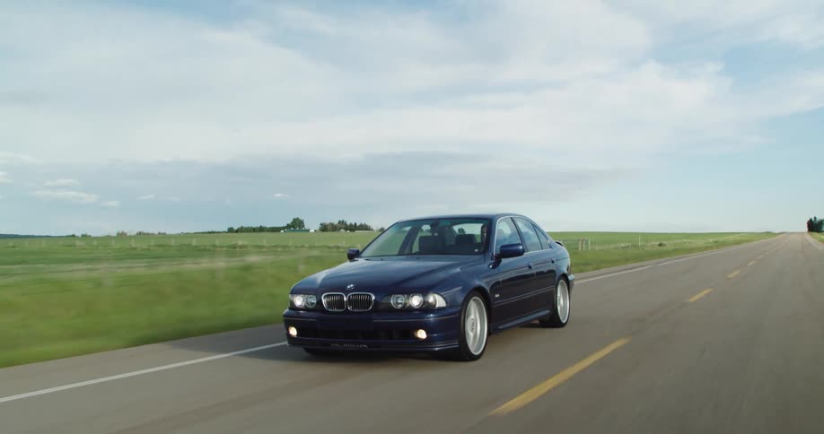 A car travels along a road through a grassy countryside during the day