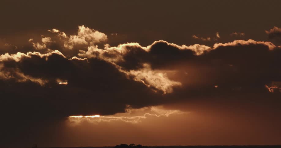 Cumulus clouds in a darkening sky as the sunlight shines around the edges of the clouds