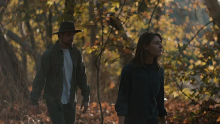 A man and woman are walking through a forest in the daytime during the fall season