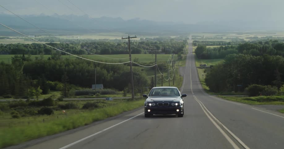 A vehicle drives past open fields and tree lines on a rural highway