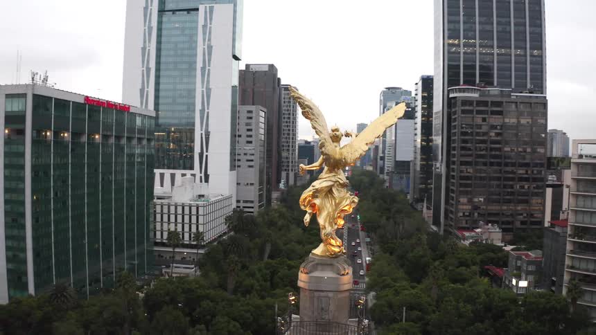 A gold statue of a human with wings sits high above the ground near tall skyscrapers