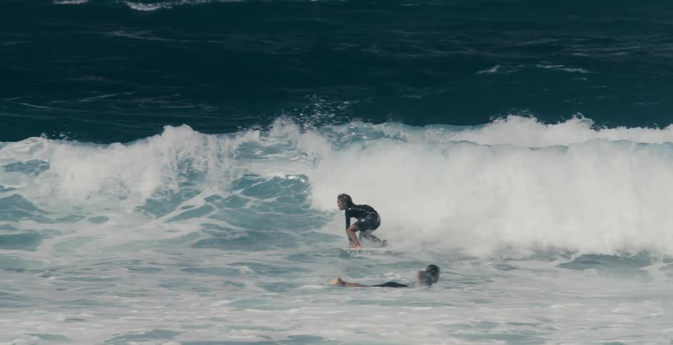 A surfer rides a curling foaming wave past another who is paddling out