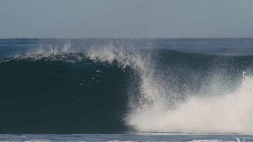 Male surfer with long hair and wetsuit rides big ocean wave