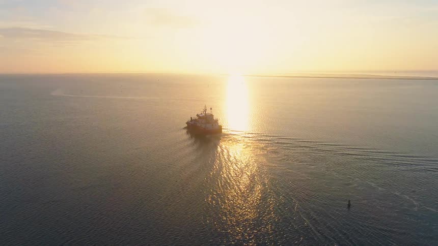 A boat is sailing across the water as the sun is setting on the horizon