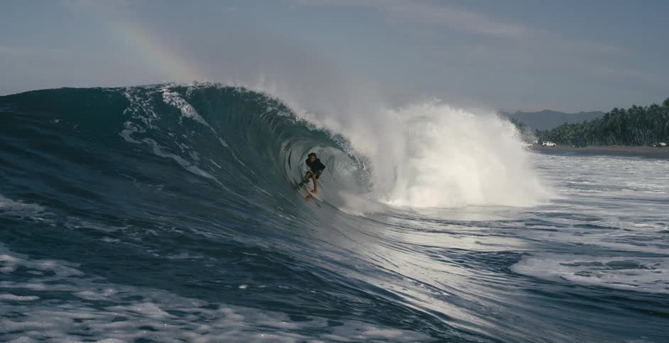 Teen surfer with long hair and wetsuit rides big ocean wave