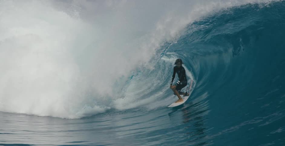 A surfer lowers his stance while riding a tall wave