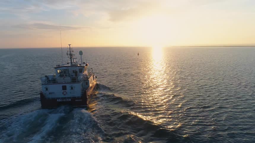Aerial view of boat traveling across the sea at sunrise