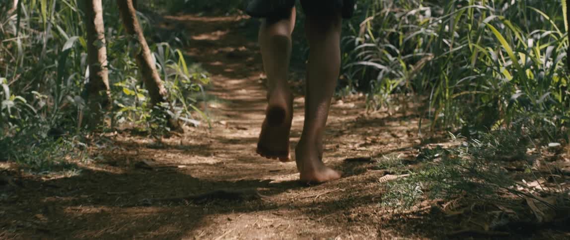A person is running barefoot on the dirt trail