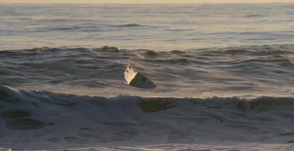 A strong wave and wind tosses a boogie board in the sea