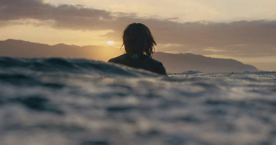A surfer bobs up and down with the water at sunset