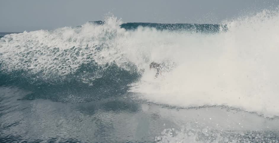 Teen surfer with long hair and wetsuit rides on ocean wave